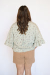 Person wearing a light-colored floral blouse and beige shorts 