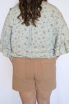 Person wearing a floral blouse and beige shorts 