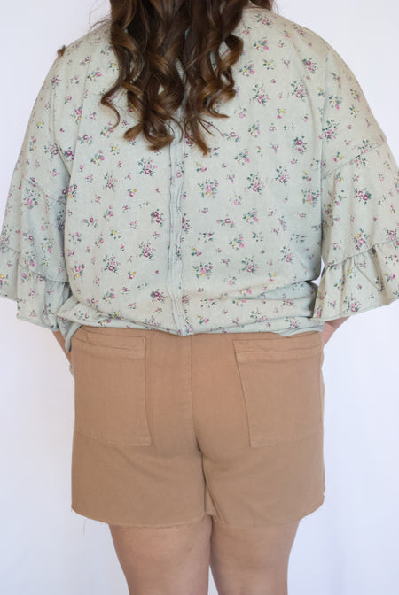 Person wearing a floral blouse and beige shorts 
