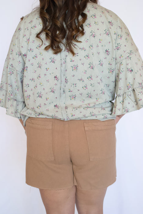 Person wearing a floral blouse and beige shorts 