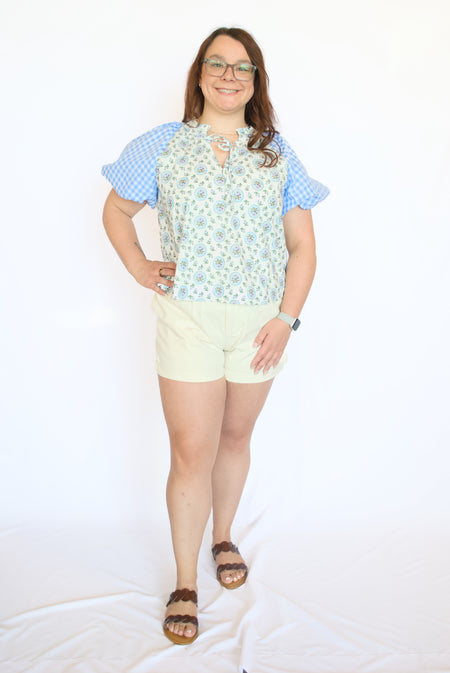 Woman wearing a floral top, checkered sleeves, and light-colored shorts 