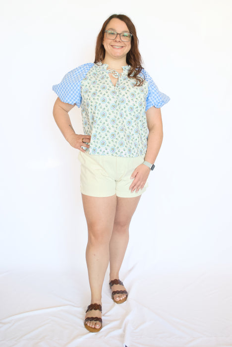 Woman wearing a floral top, checkered sleeves, and light-colored shorts 
