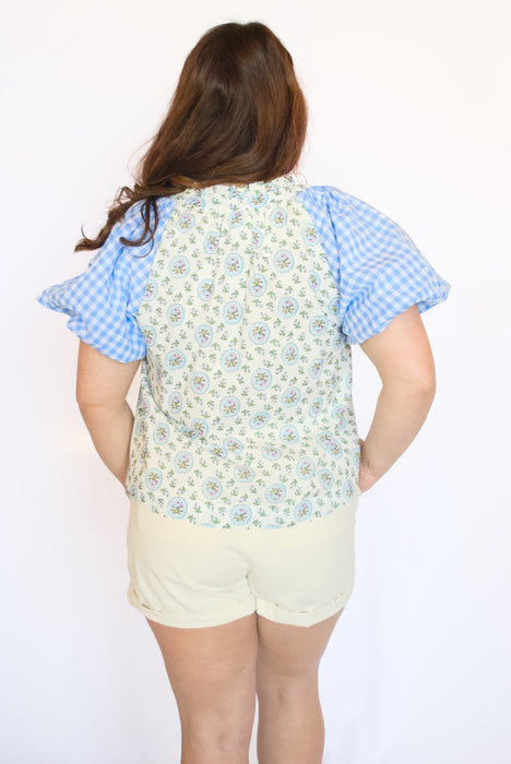 Person wearing a floral shirt with blue checkered sleeves and beige shorts 
