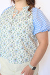 Woman wearing a floral blouse with blue checkered sleeves 