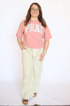 Person wearing a pink 'PRAY' t-shirt and light-colored pants 