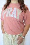 Person wearing a pink tee with 'PRAY' printed on it 