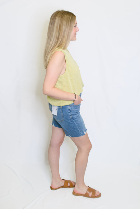 Woman wearing a light green sleeveless top and denim shorts 