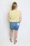 Person wearing a yellow sleeveless top and blue denim shorts 