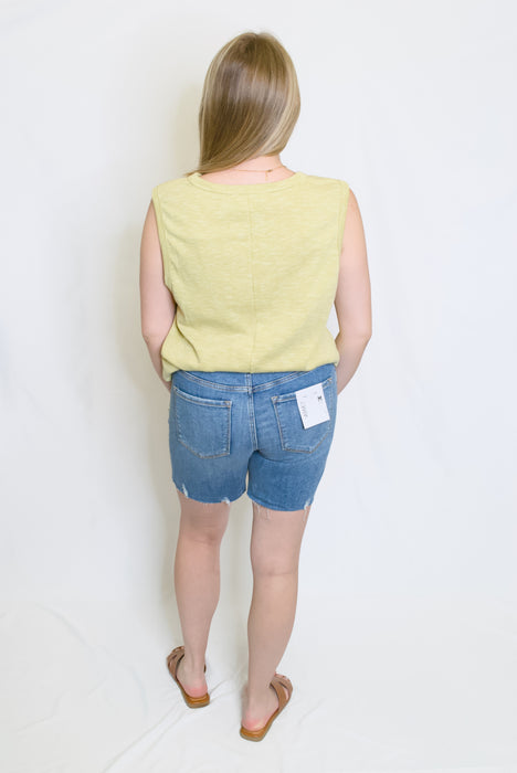 Person wearing a yellow sleeveless top and blue denim shorts 